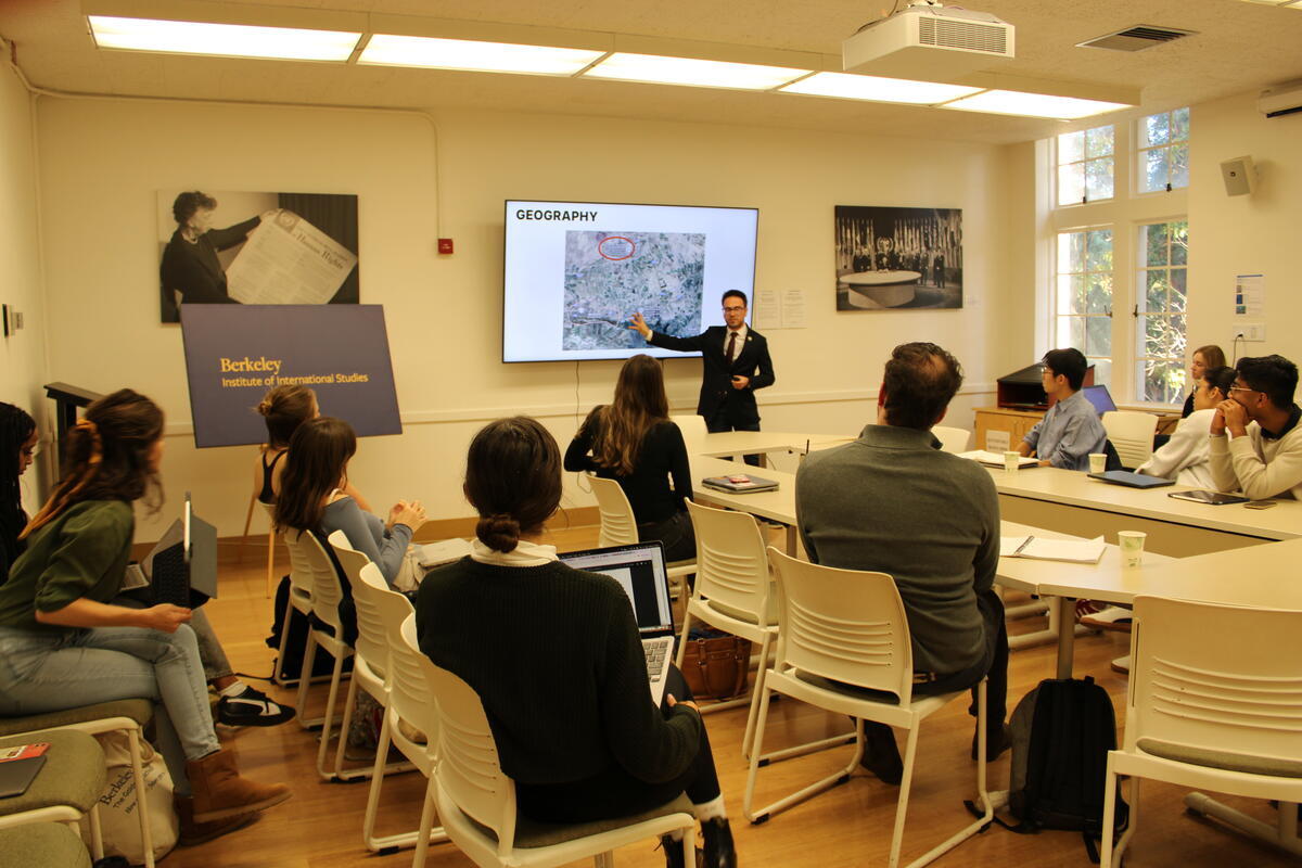 a student stands in front of their powerpoint, gesturing towards it as they present their research at the 2024  Undergraduate Conference